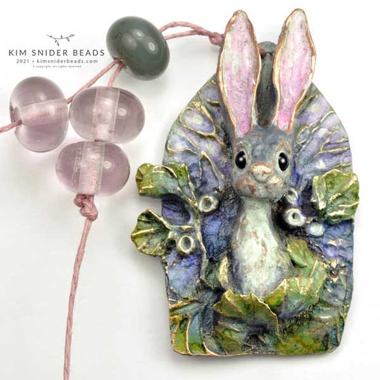 Spring bunny cathedral pendant is made with bronze. It is a one of a kind (ooak) artbead created by Kim Snider in 2021.